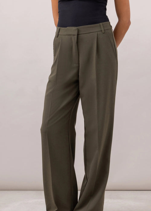 Person wearing olive green wide-leg pants and a black top on a plain background