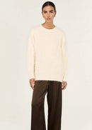 Person wearing a cream sweater and brown pants on a white background
