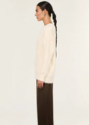 Person wearing a cream sweater and brown pants on a white background