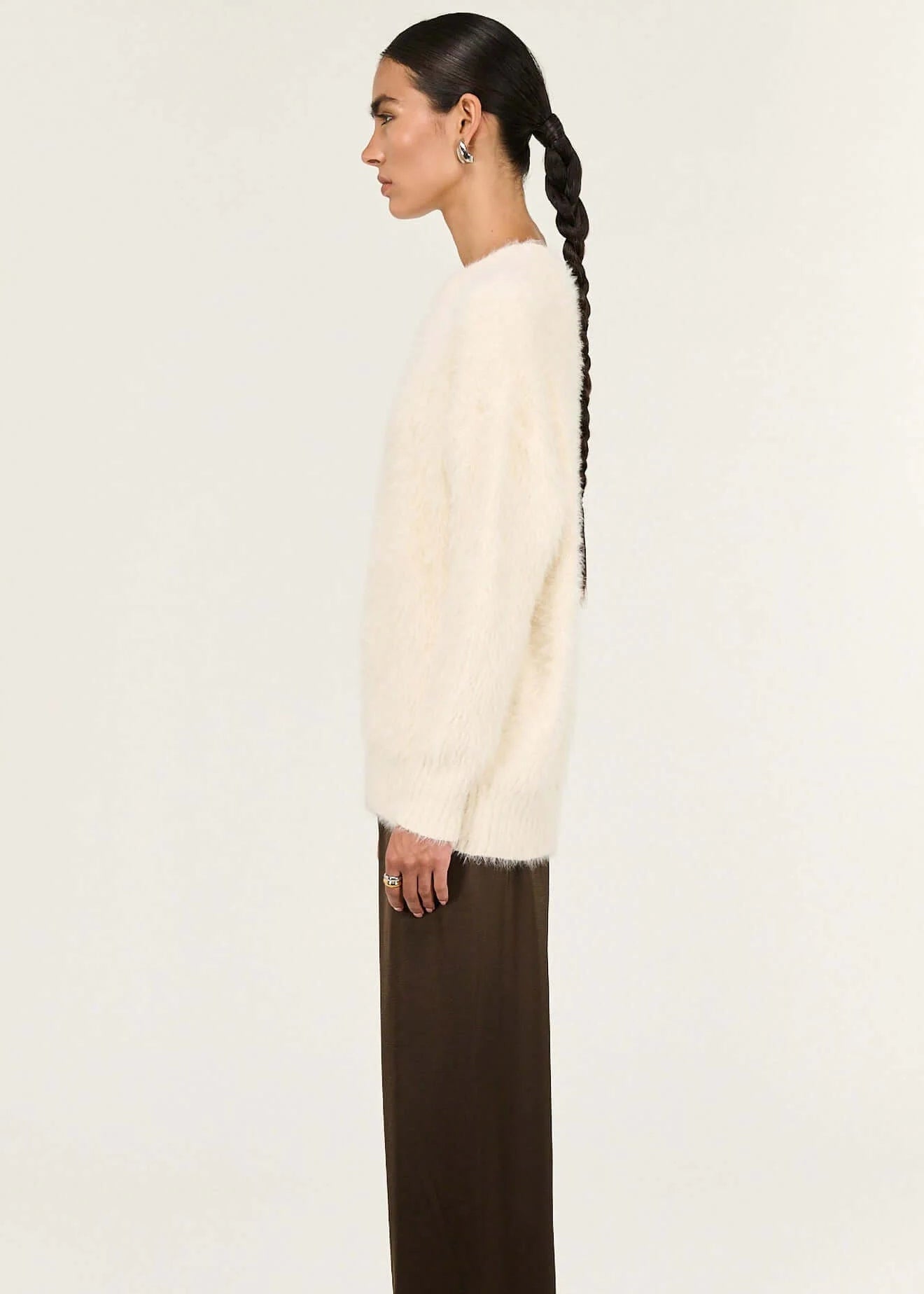 Person wearing a cream sweater and brown pants on a white background