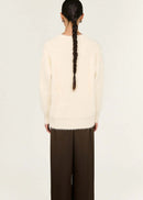 Person wearing a cream sweater and brown pants on a white background