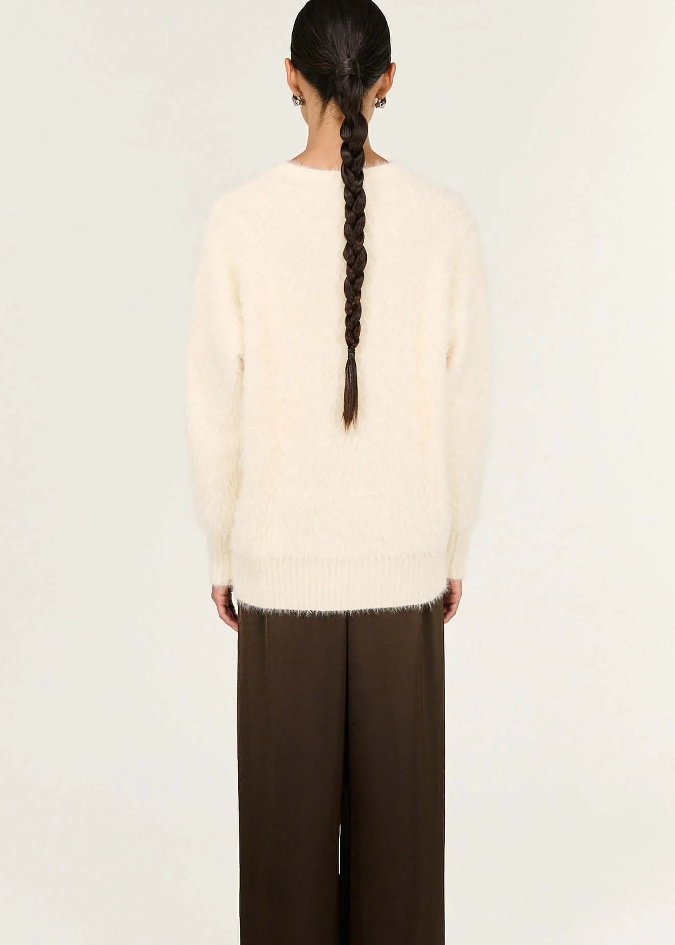 Person wearing a cream sweater and brown pants on a white background