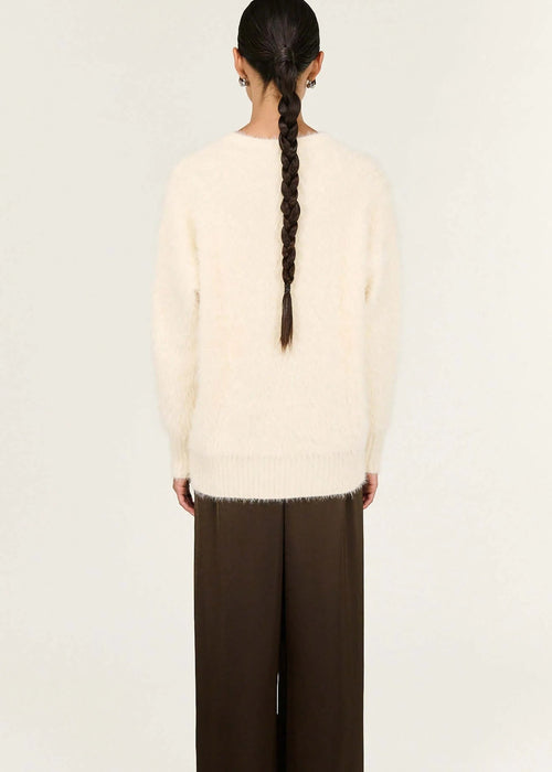 Person wearing a cream sweater and brown pants on a white background