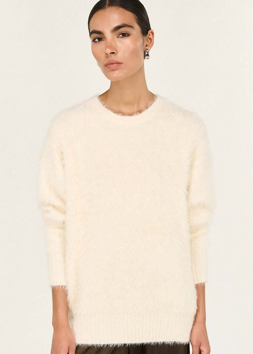 Person wearing a cream sweater and brown pants on a white background