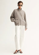 Person wearing a beige jacket and white pants on a white background