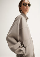 Person wearing a beige jacket and white pants on a white background