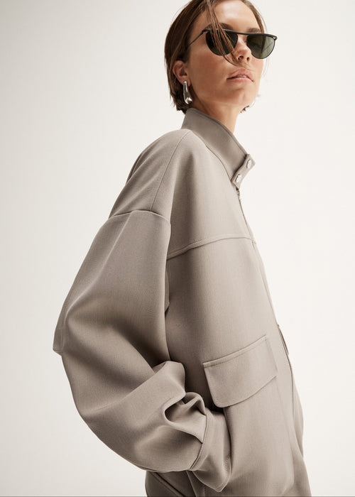 Person wearing a beige jacket and white pants on a white background