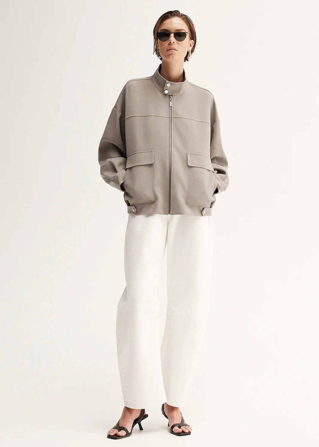 Person wearing a grey jacket and white pants on a white background