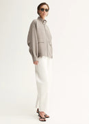 Person wearing a grey jacket and white pants on a white background