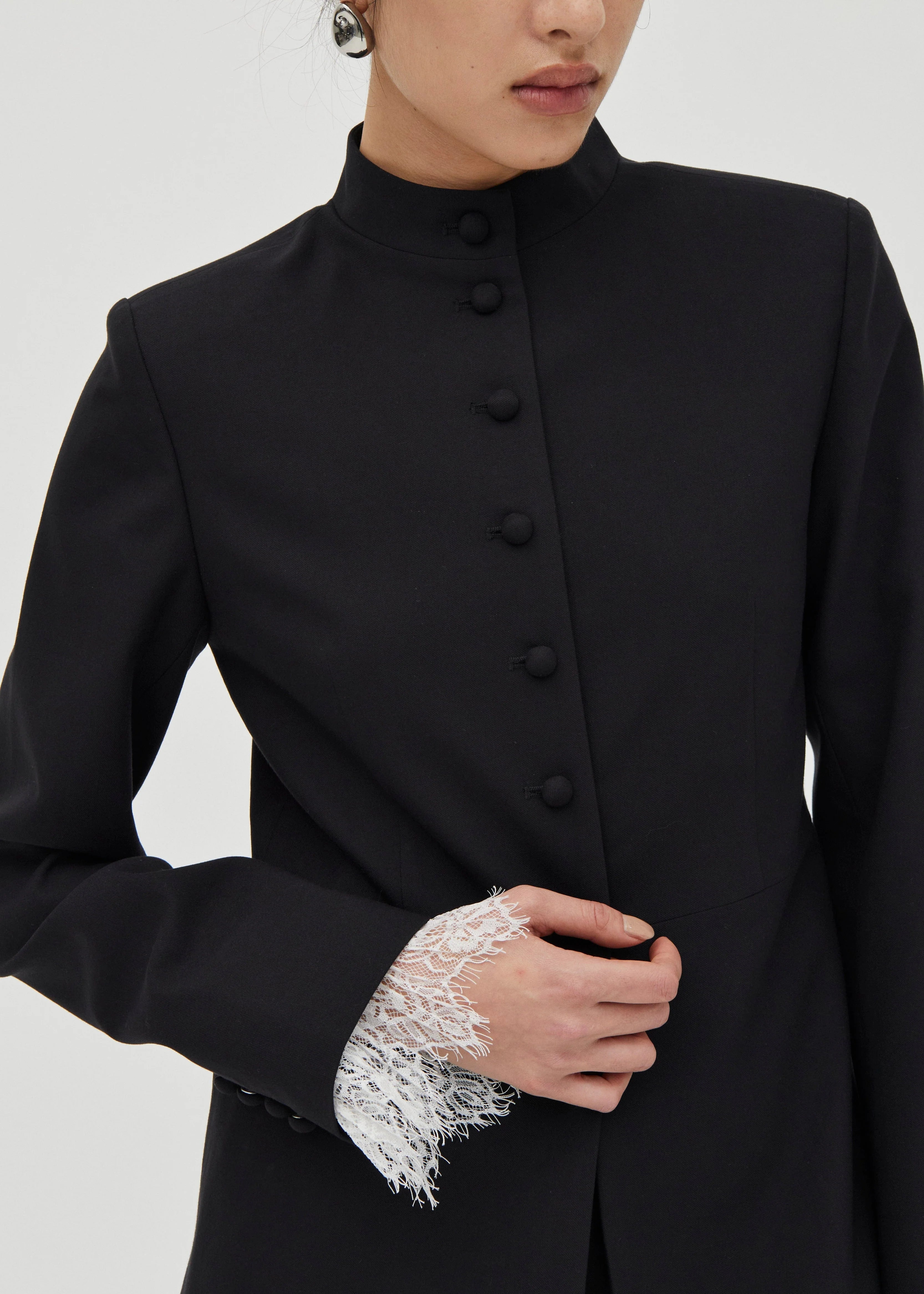 Black coat with lace cuffs worn by a person on a white background