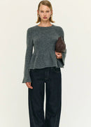Woman wearing a grey top and dark pants holding a brown clutch against a white background