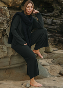 Woman in dark green outfit sitting on rocks by a stone wall