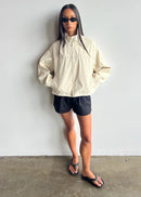 Person wearing a beige jacket and black shorts against a white background