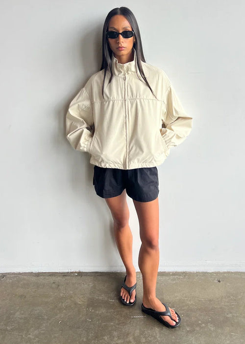 Person wearing a beige jacket and black shorts against a white background