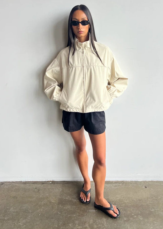 Person wearing a beige jacket and black shorts against a white background