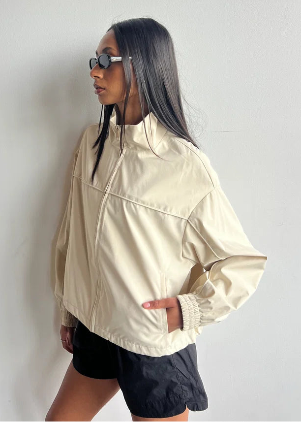 Person wearing a beige jacket and black shorts against a white background