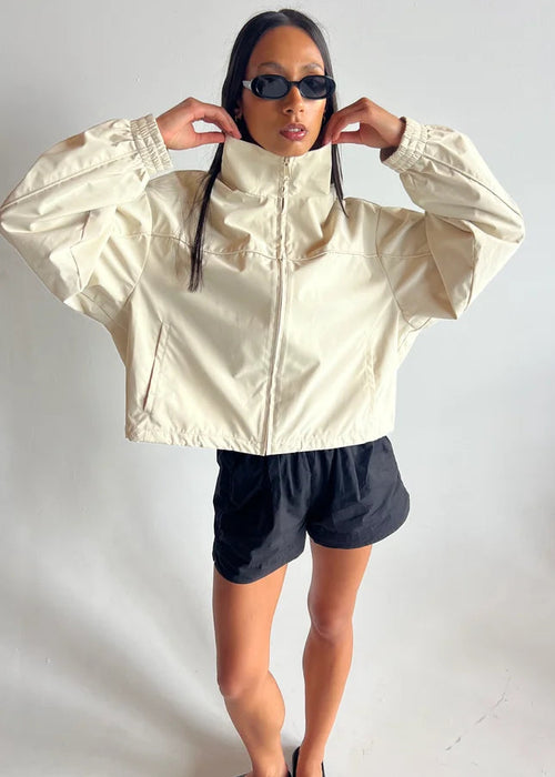 Person wearing a beige jacket and black shorts against a white background