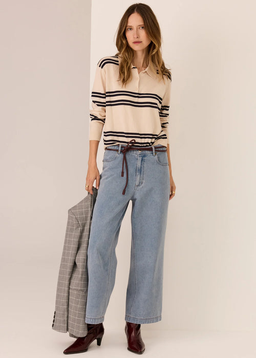 Woman wearing a striped sweater and jeans, holding a plaid jacket, on a plain background
