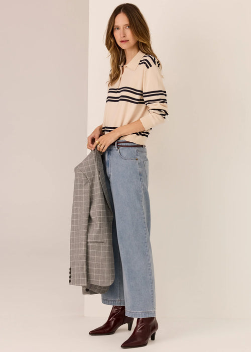 Woman wearing a striped sweater and jeans, holding a plaid jacket, on a plain background