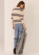 Woman wearing a striped sweater and jeans, holding a plaid jacket, on a plain background