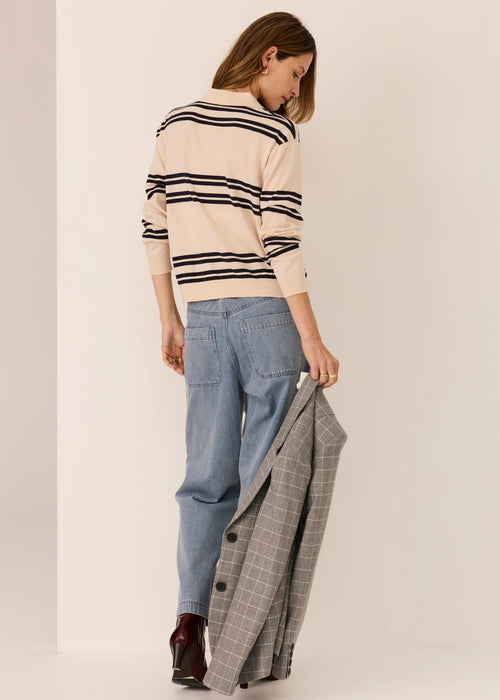 Woman wearing a striped sweater and jeans, holding a plaid jacket, on a plain background