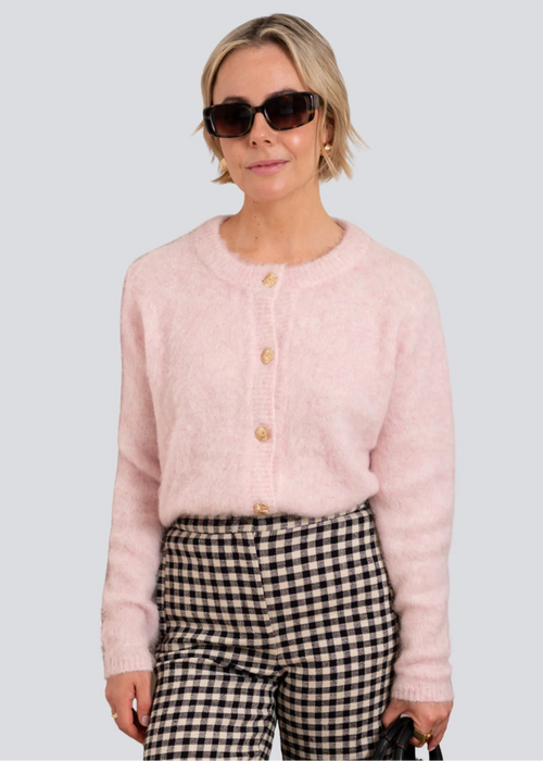 Woman wearing a pink cardigan and checkered pants with sunglasses on a light grey background
