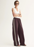 Woman wearing a white sleeveless top and purple pants with white stripes on a white background