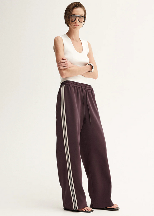Woman wearing a white sleeveless top and purple pants with white stripes on a white background