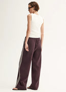 Woman wearing a white sleeveless top and purple pants with white stripes on a white background