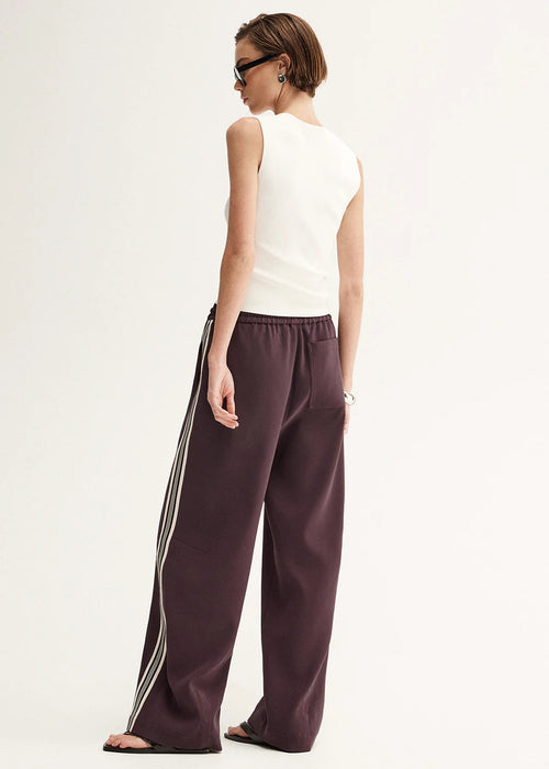 Woman wearing a white sleeveless top and purple pants with white stripes on a white background