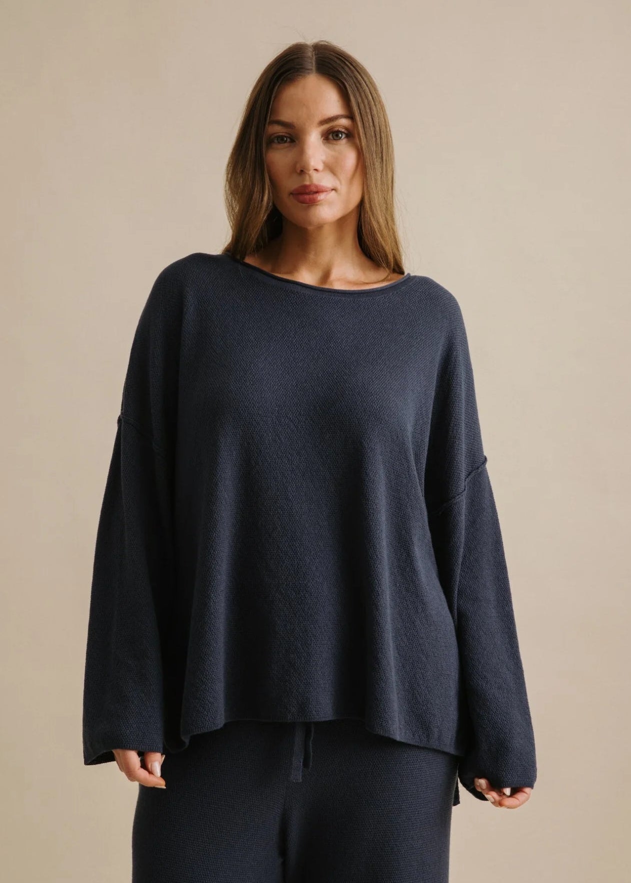 Woman wearing a navy blue sweater and pants against a beige background