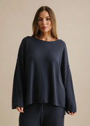 Woman wearing a navy blue sweater and pants against a beige background
