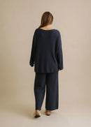 Woman wearing a navy blue sweater and pants against a beige background