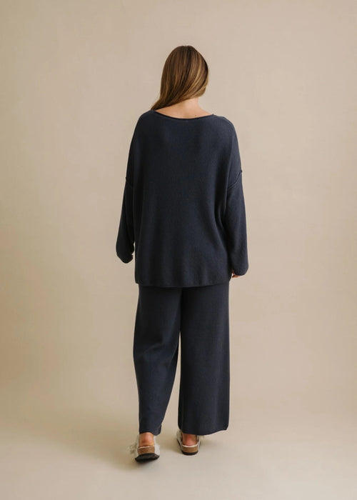 Woman wearing a navy blue sweater and pants against a beige background