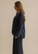 Woman wearing a navy blue sweater and pants against a beige background