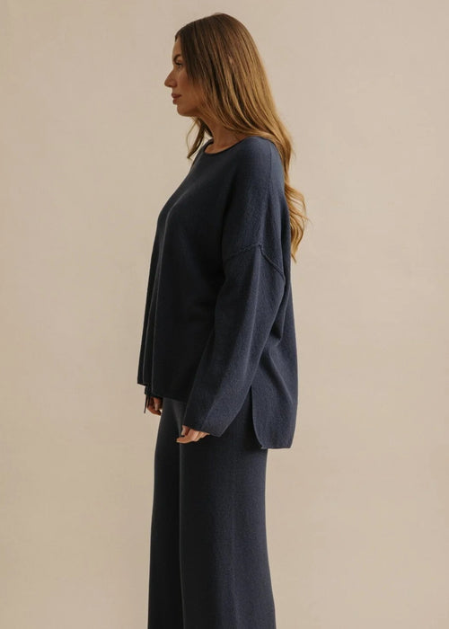 Woman wearing a navy blue sweater and pants against a beige background