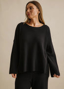 Woman wearing a black top and pants against a beige background