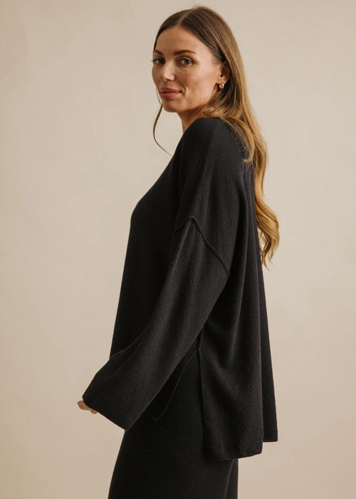 Woman wearing a black top and pants against a beige background