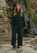 Woman in dark green outfit standing on rocky terrain with a natural background