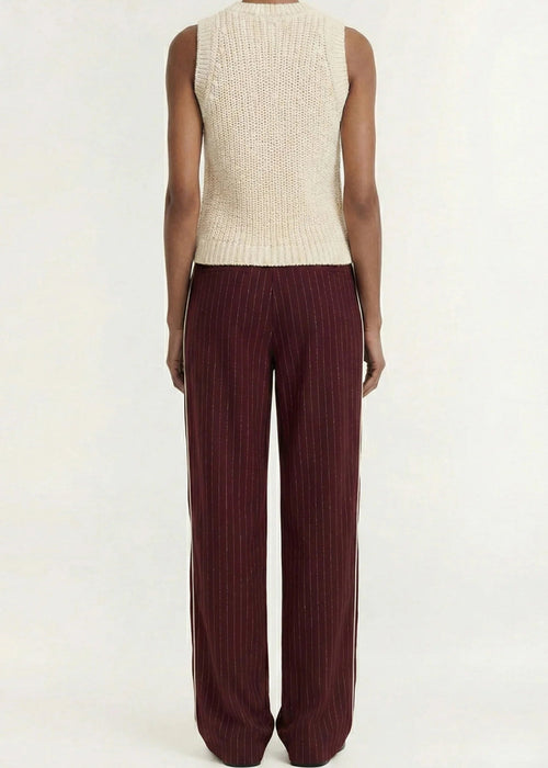 A model shown from the back wearing a cream ribbed sleeveless knit top and dark burgundy wide-leg pleated trousers, set against a plain light gray studio background.