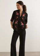 Woman wearing a black floral embroidered shirt and black pants against a white background