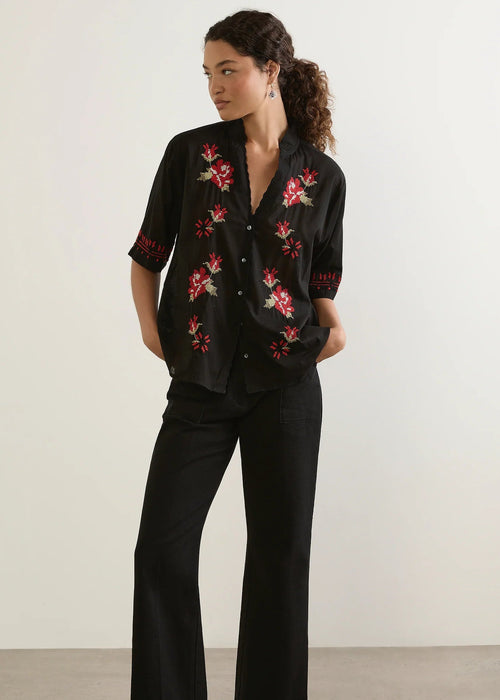 Woman wearing a black floral embroidered shirt and black pants against a white background