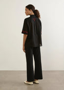 Woman wearing a black floral embroidered shirt and black pants against a white background