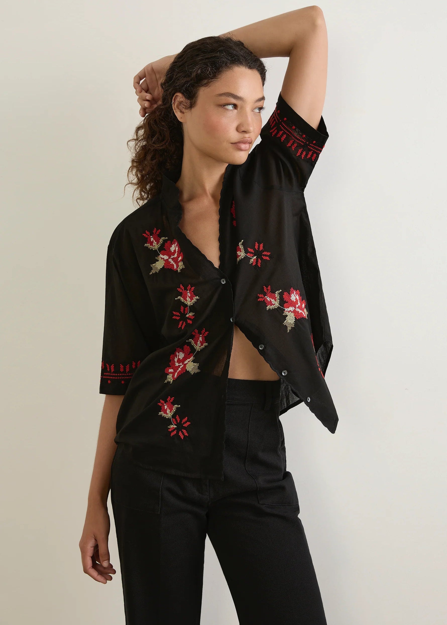 Woman wearing a black floral embroidered shirt and black pants against a white background