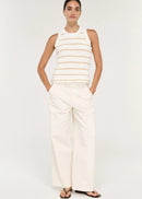 A model stands against a plain light background wearing a sleeveless knit top with thin horizontal beige stripes on an off-white base, paired with off-white wide-leg pants and black sandals.