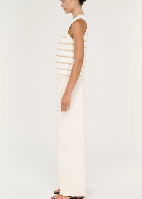 A model stands against a plain light background wearing a sleeveless knit top with thin horizontal beige stripes on an off-white base, paired with off-white wide-leg pants and black sandals.