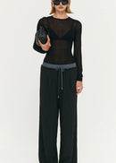 Model wearing a black outfit with sheer top and wide-leg pants on a white background