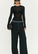 Model wearing a black outfit with sheer top and wide-leg pants on a white background