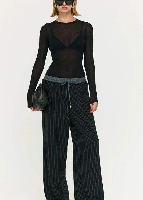 Model wearing a black outfit with sheer top and wide-leg pants on a white background