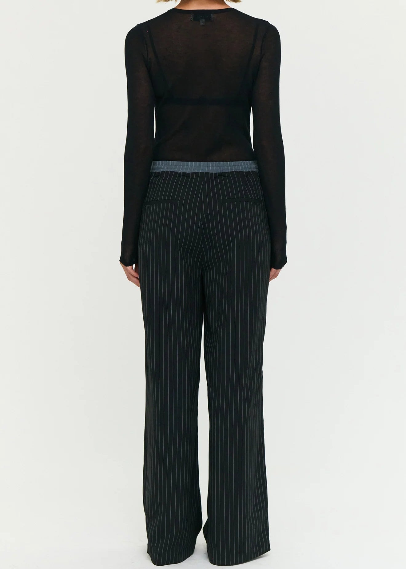 Model wearing a black outfit with sheer top and wide-leg pants on a white background